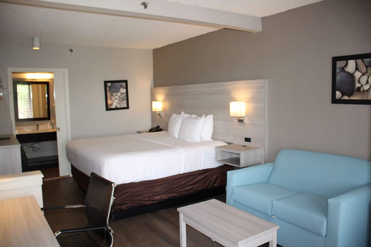 Quarto de hotel com cama, escrivaninha, cadeira, mesinha e sofá azul claro.