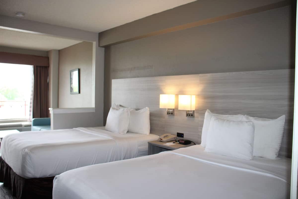Quarto de hotel com duas camas, uma mesa de cabeceira, um telefone e uma luminária fixada na parede.