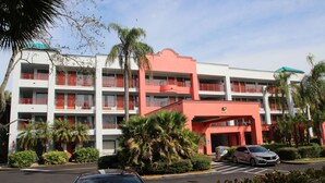 Un hotel de varios pisos con balcones, palmeras y un estacionamiento.