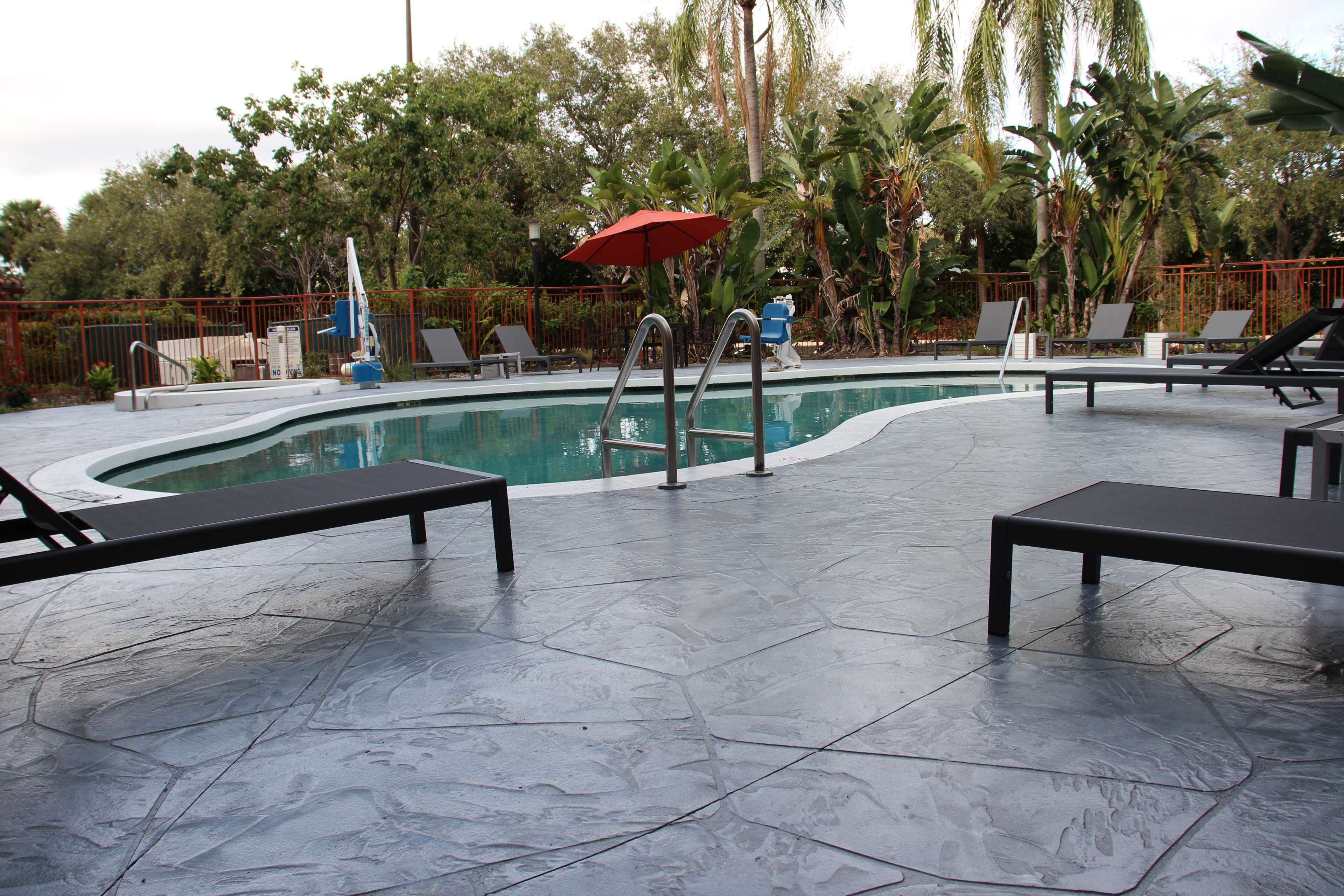 A swimming pool with a red umbrella, metal pool ladder, and lounge chairs.