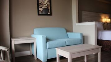 Una habitación de hotel moderna con un sofá azul claro, una mesita blanca pequeña y una cama con cabecera de madera.