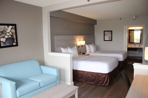 A hotel room with two beds, a light blue sofa, a wooden table, and a bathroom visible through an open door. - Boca Suites Deerfield Beach, SureStay Collection by BW (Deerfield Beach)