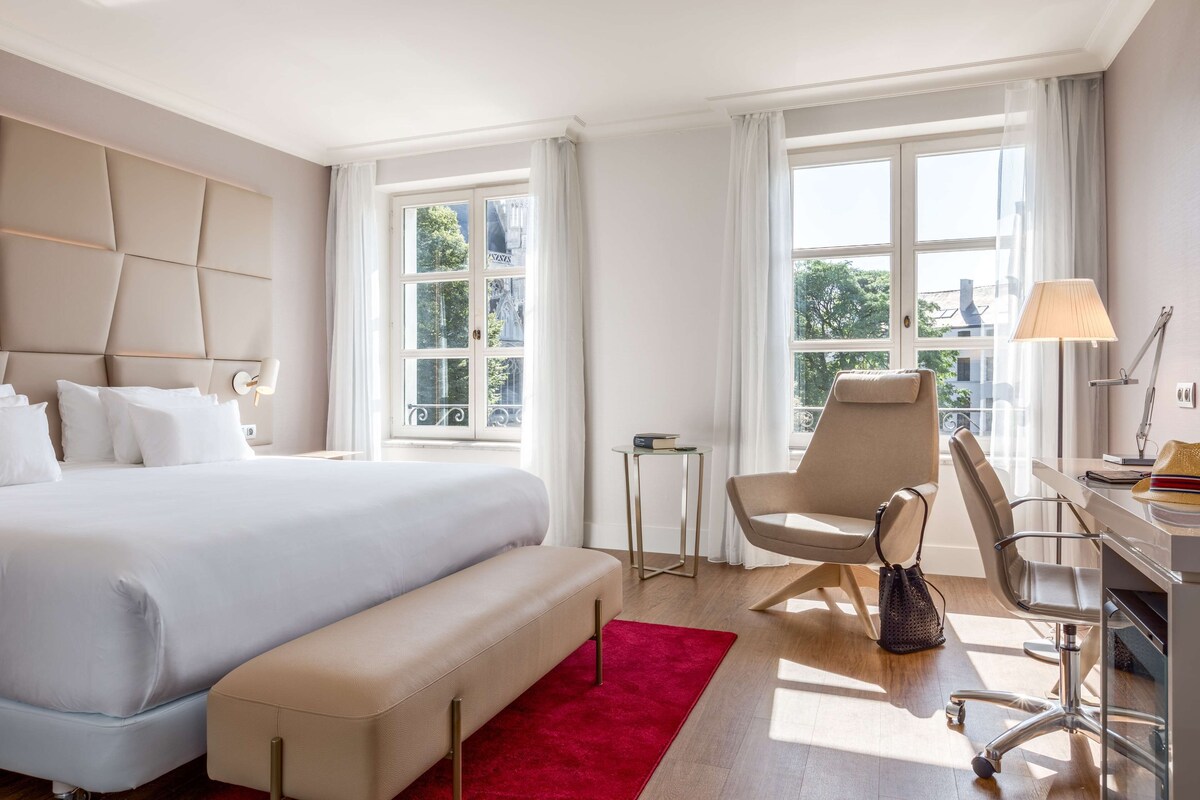 Una camera d'albergo con un letto grande, una scrivania con una sedia, un tavolino e una panca.