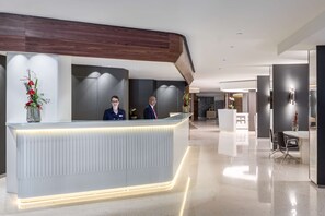 A modern reception desk with a lighted edge, a reception area, and a seating area with a table and chairs. - NH Collection Brussels Grand Sablon (Brussels)