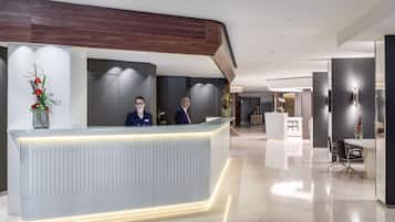 Un comptoir d’accueil moderne doté d’un bord illuminé, un espace d’accueil et un coin salon avec une table et des chaises.