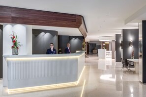 A modern reception desk with a lighted edge, a reception area, and a seating area with a table and chairs. - NH Collection Brussels Grand Sablon (Brussels)