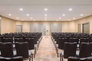 Une salle de conférence avec des rangées de chaises, un pupitre et des portes.
