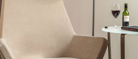 Una silla moderna con respaldo alto, una mesa redonda con una lámpara y una botella de vino.