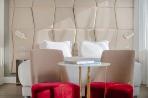 Una camera d'albergo moderna con un letto grande, due poltrone rosse, un tavolino rotondo e un lampadario a parete.