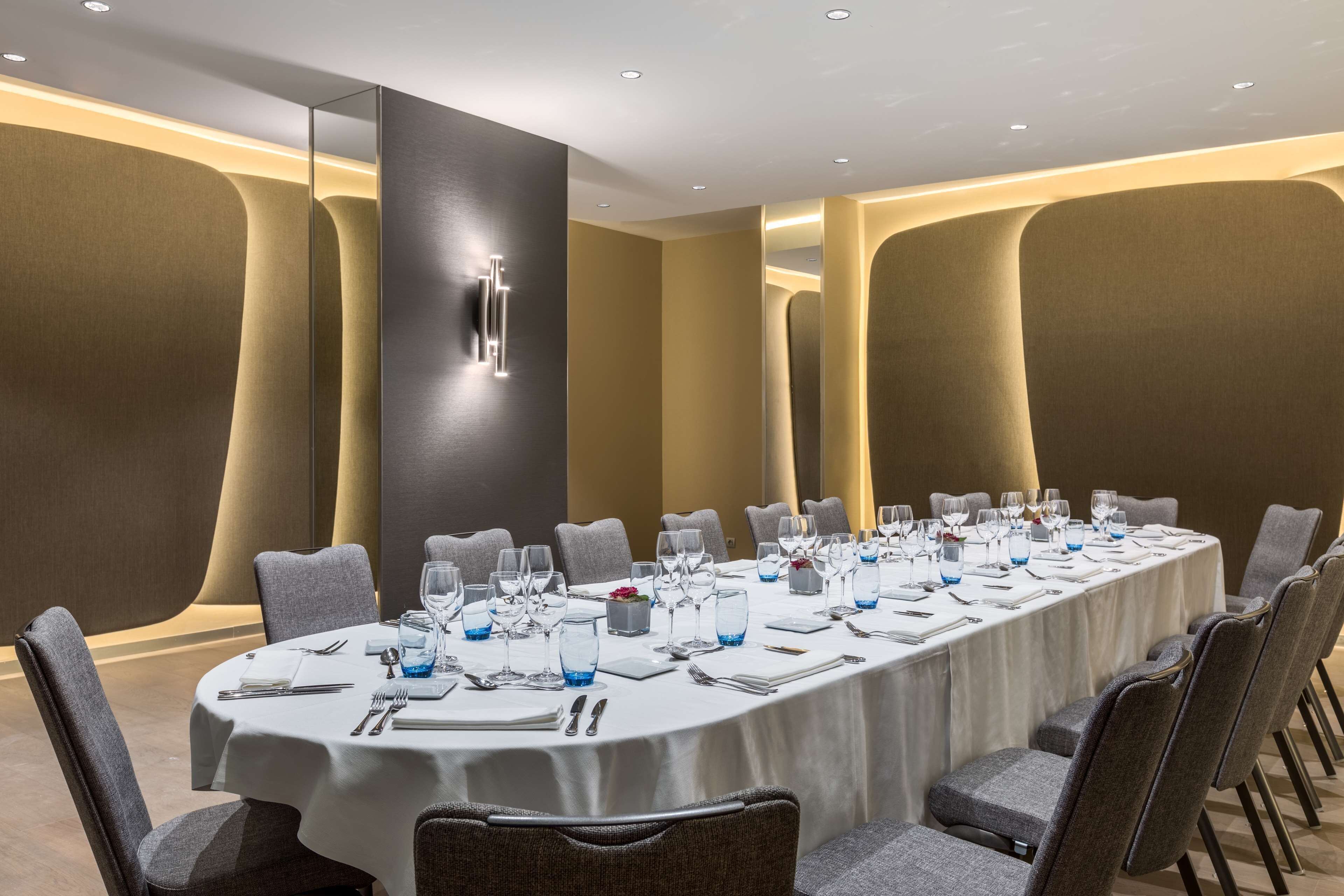 Un salón de conferencias con una larga mesa dispuesta para una reunión, rodeado de sillas.