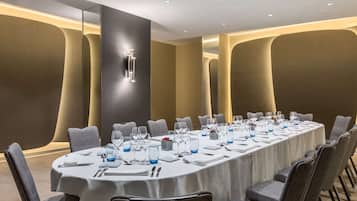 Een vergaderzaal met een lange tafel, gedekt voor een vergadering, omringd door stoelen.