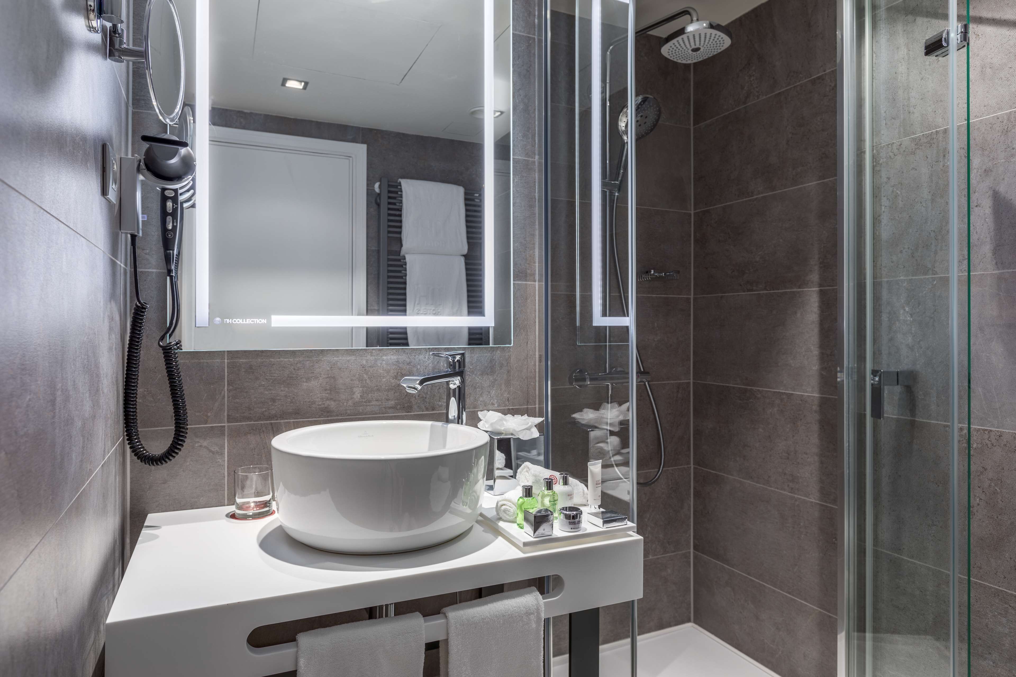 Une salle de bain moderne avec un grand lavabo blanc, une douche en verre et un miroir doté d’un porte-serviettes.