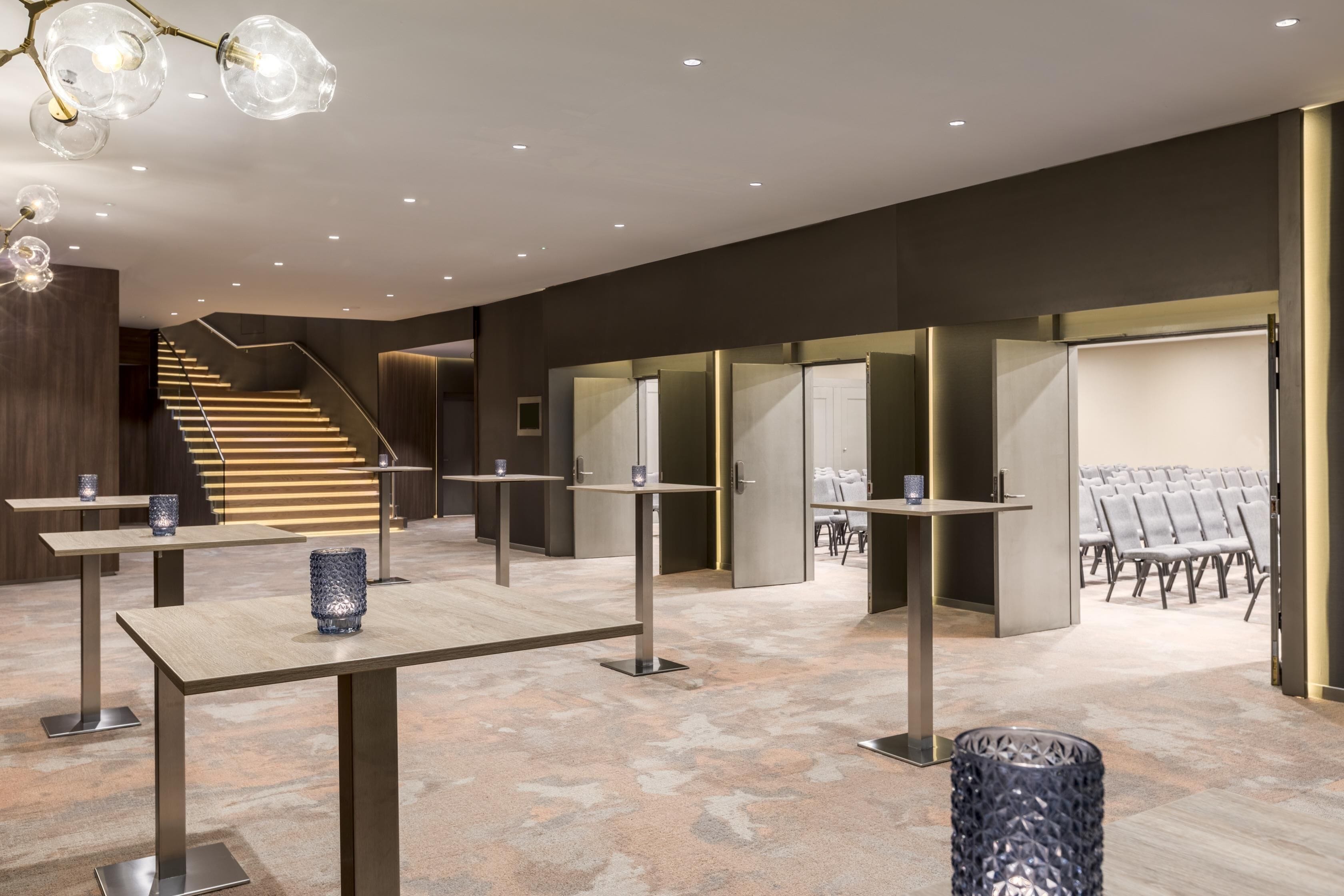 Un hall d’hôtel moderne avec un escalier, des espaces de détente et un comptoir d’accueil.