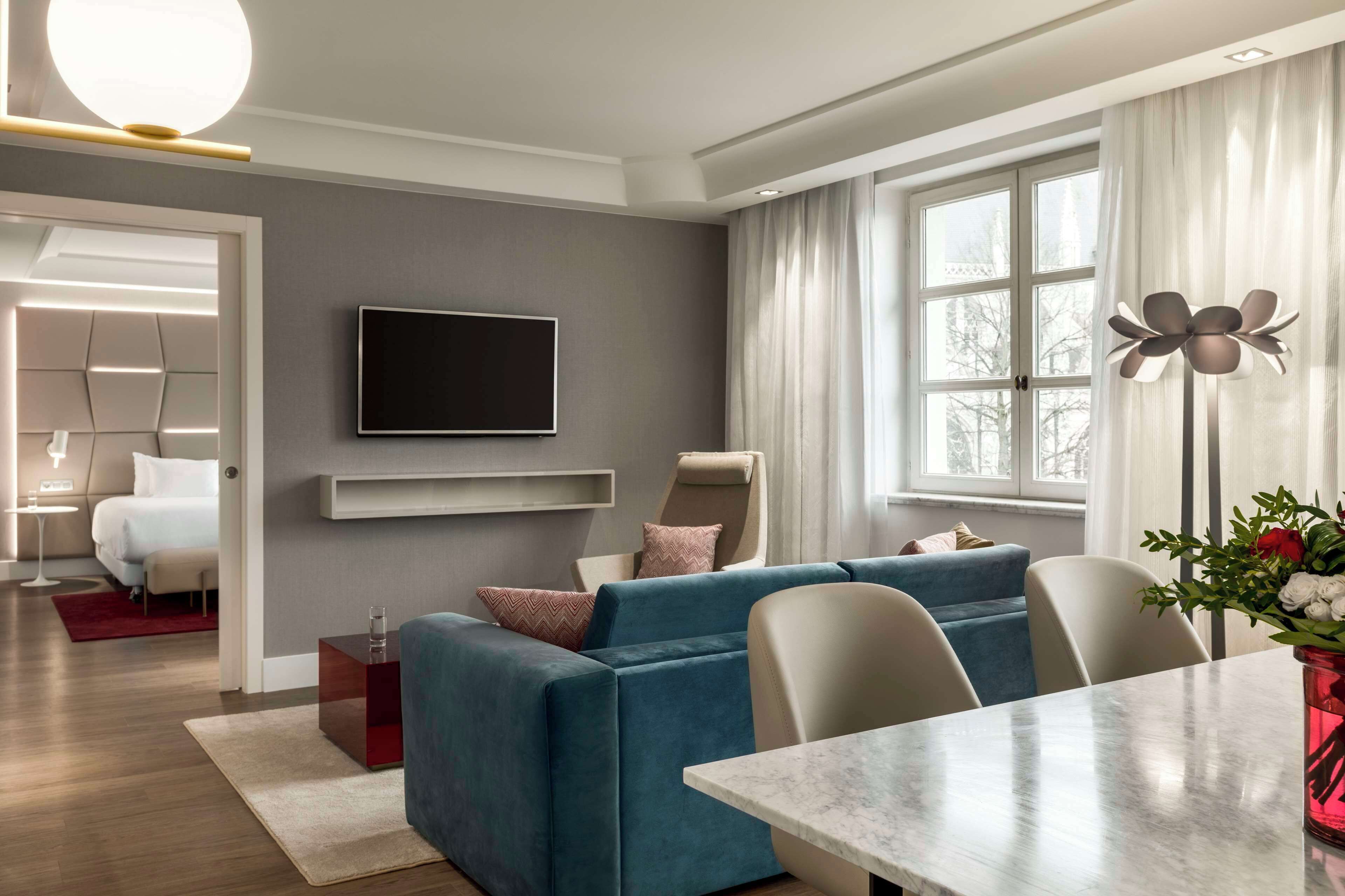 Uma sala de estar moderna com sofá, televisão de tela plana, mesa de jantar e uma grande janela com cortinas.