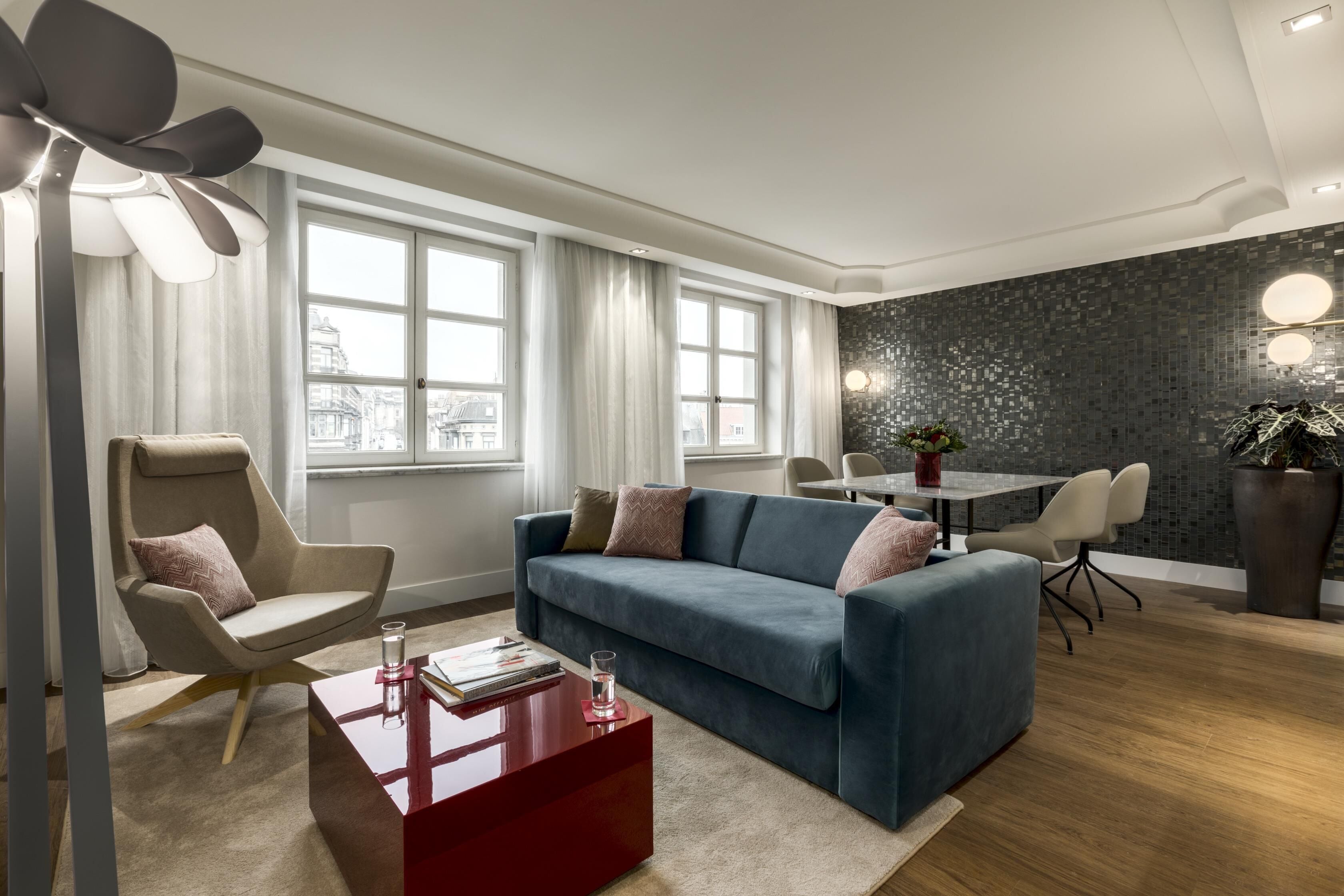 Uma sala de estar moderna com um sofá azul, uma mesa de centro vermelha e um espaço de jantar com mesa e cadeiras.