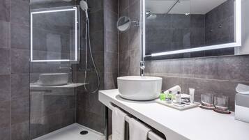 Uma casa de banho moderna com chuveiro envolto em vidro, lavatório branco e espelho com iluminação integrada.