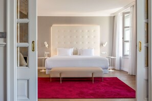 Ein Schlafzimmer mit einem großen Bett, Nachttischen, einer Bank und einem roten Teppich.