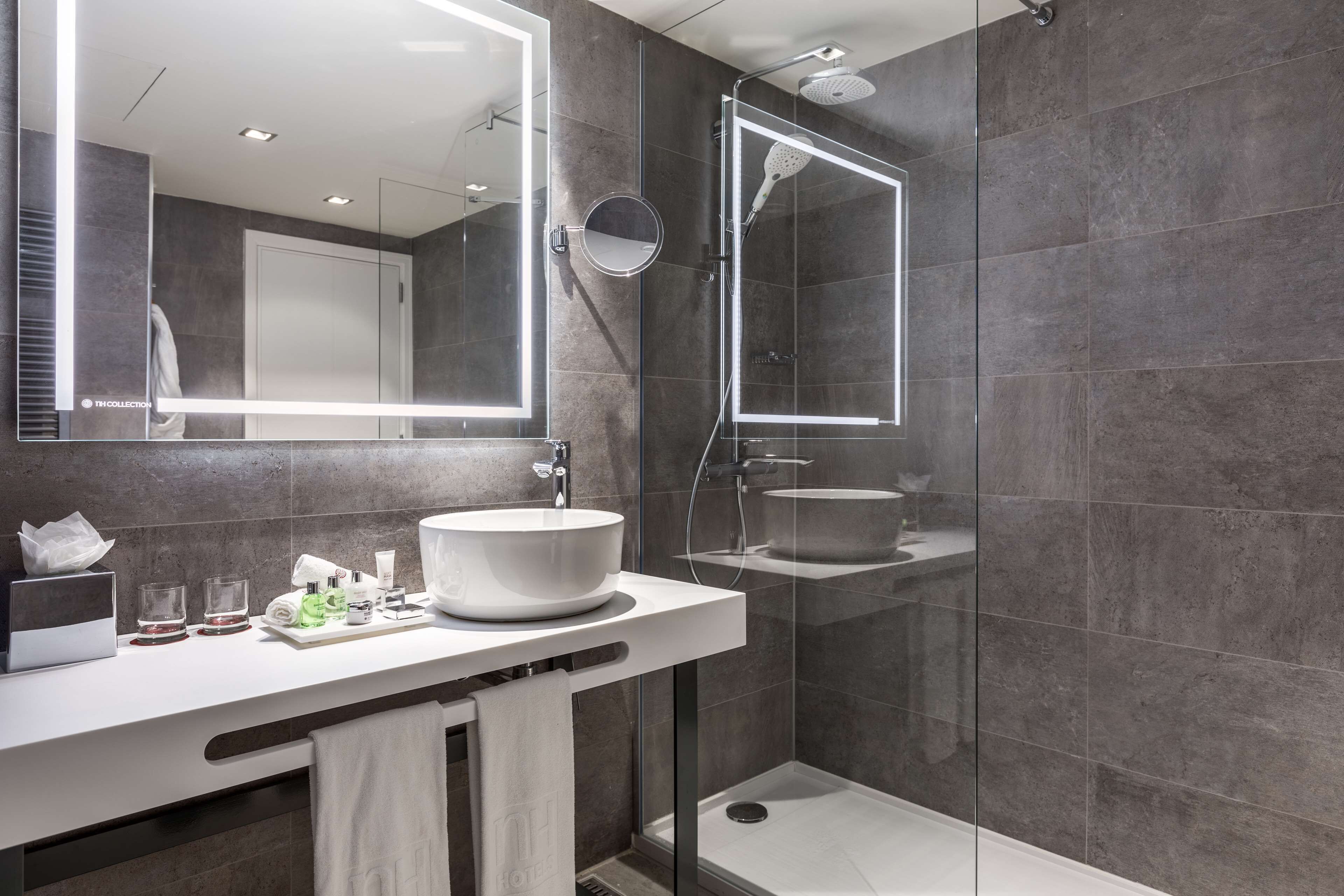 Un baño moderno con un espejo grande, un lavamanos sobre encimera y una ducha con mampara de vidrio.