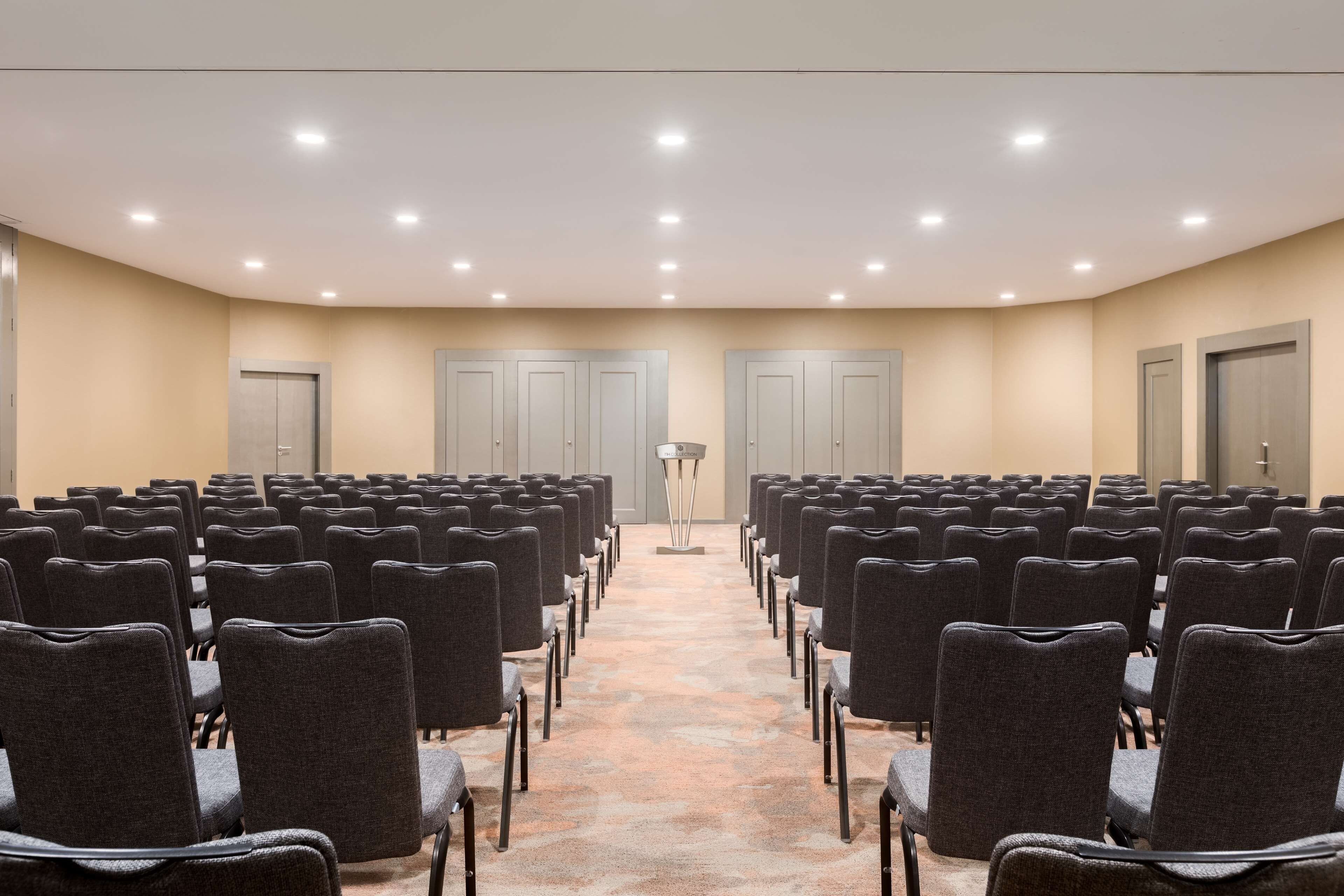 A conference room with rows of chairs, a podium, and doors.
