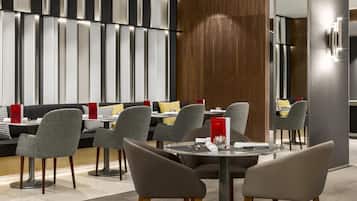 Um restaurante moderno com cadeiras estofadas em cinza, uma parede de destaque em madeira e um suporte de menu vermelho.