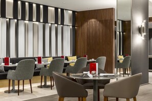 A modern restaurant with grey upholstered chairs, a wooden accent wall, and a red menu stand. - NH Collection Brussels Grand Sablon (Brussels)