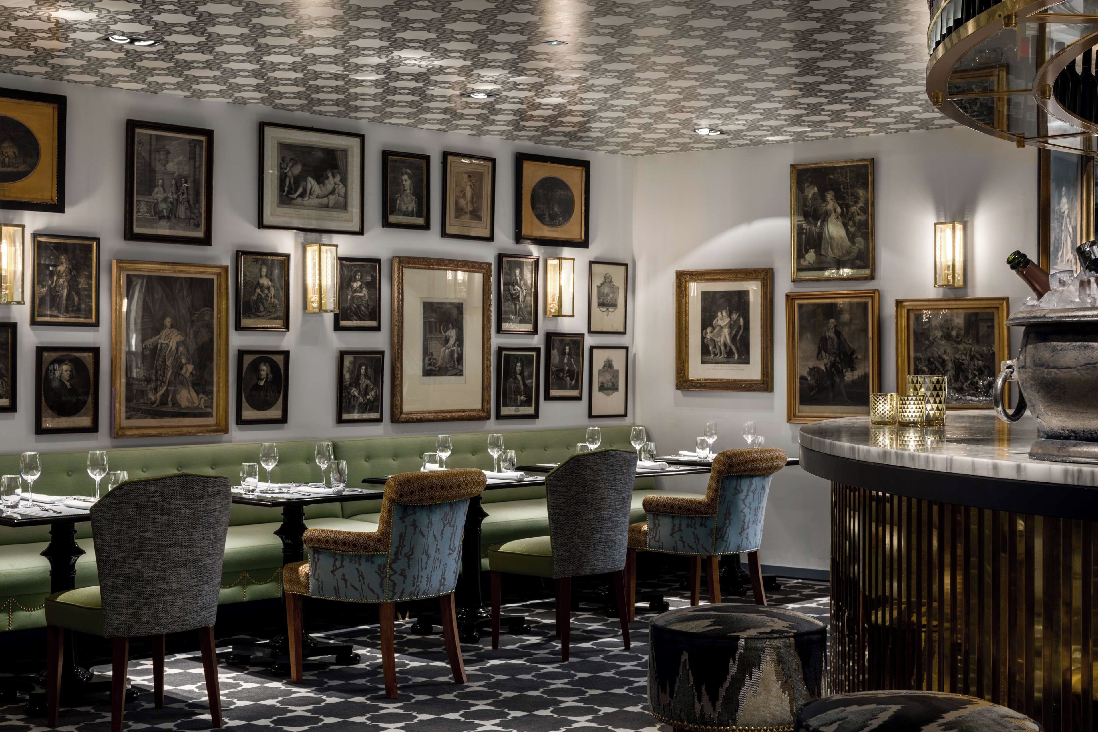 A dining area with a patterned floor, green upholstered seating, and framed artwork on the walls.