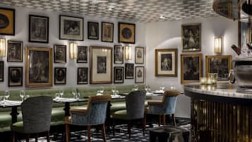 A dining area with a patterned floor, green upholstered seating, and framed artwork on the walls.