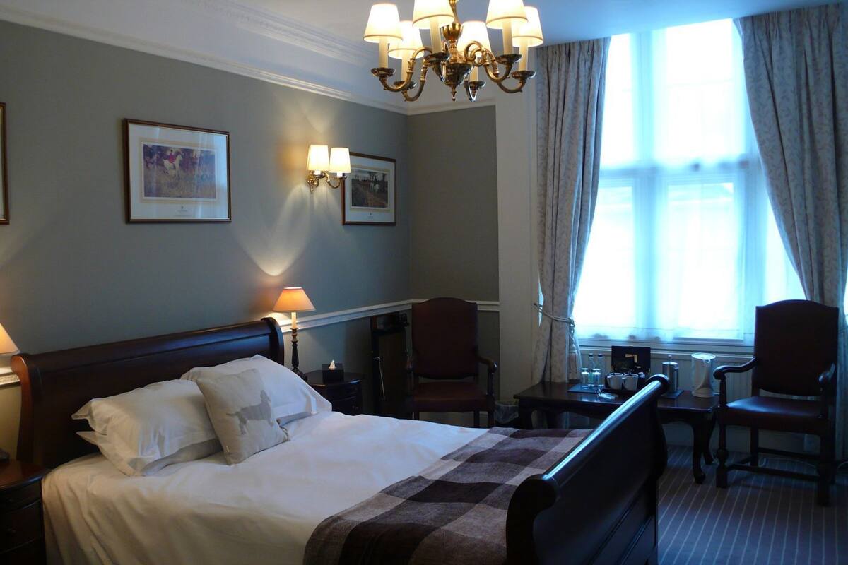 Une chambre d’hôtel comprenant un lit, des lampes de chevet, un bureau avec une chaise et une fenêtre avec des rideaux.