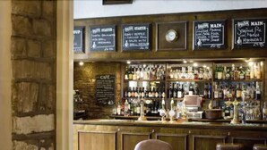 Zona de bar con pared de piedra, mostrador de madera y varios taburetes.