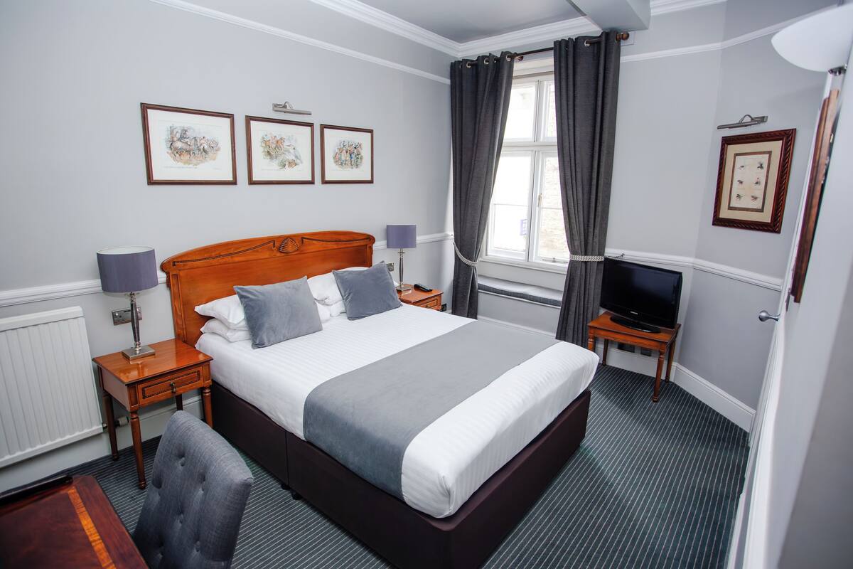 Une chambre d’hôtel avec un grand lit, deux tables de chevet, une télévision et des œuvres d’art encadrées accrochées aux murs.
