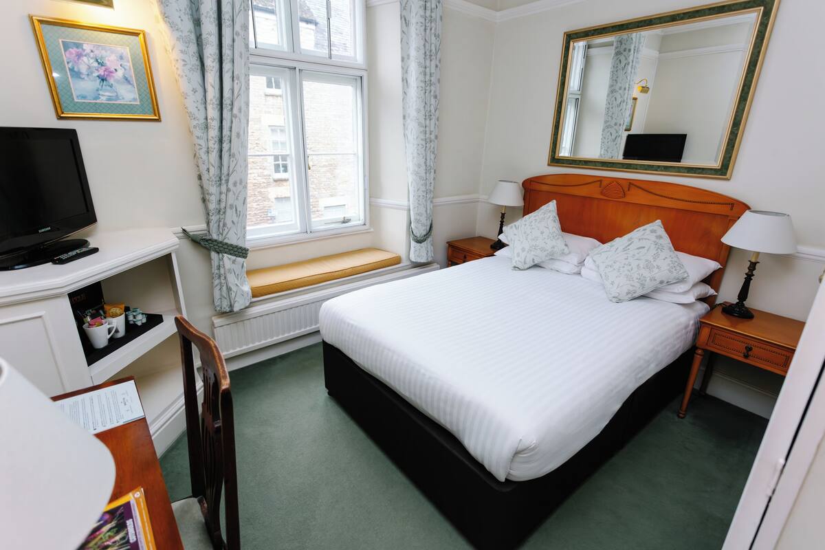 Une chambre d’hôtel comprenant un lit, une télévision, un bureau avec une chaise, une fenêtre avec des rideaux et un miroir au mur.