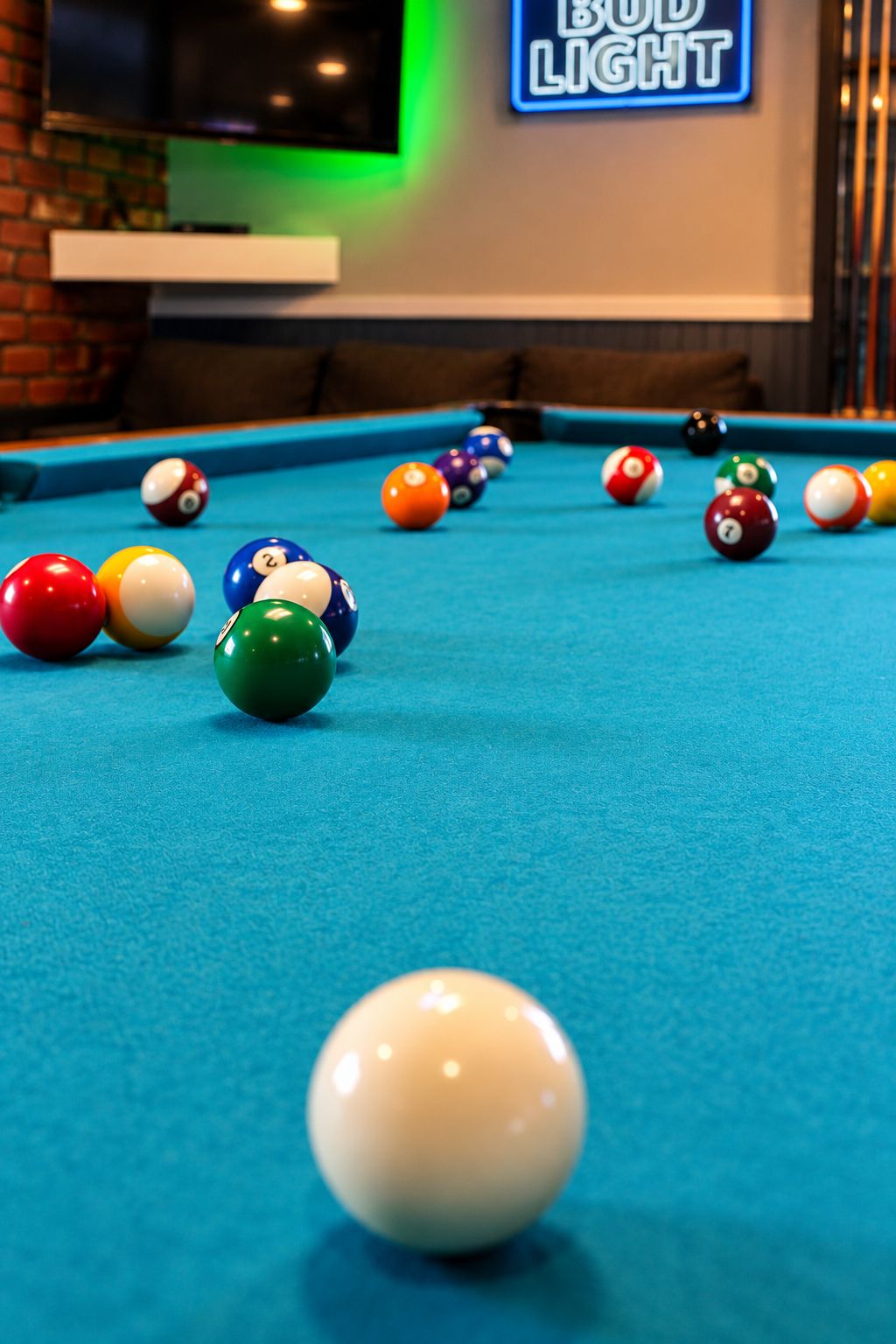 A pool table with various colored balls and a neon sign in the background.