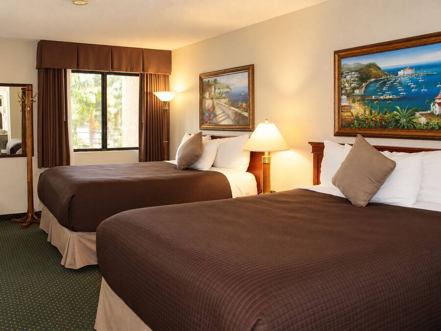 Una habitación de hotel con dos camas, un ventanal grande, un cuadro y un espejo.