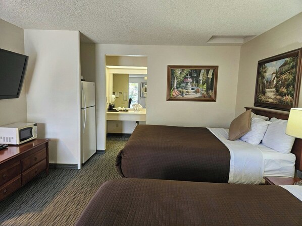 A hotel room with a bed, a desk with a microwave, a television, and a painting on the wall.