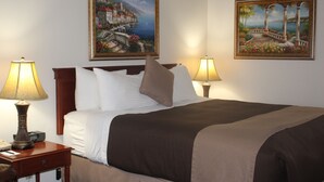 A neatly made bed with white and brown linens, two bedside lamps, and two framed paintings on the wall.