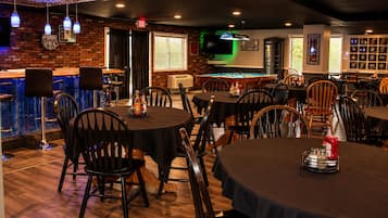 A bar area with tables and chairs, a pool table, and a brick wall with a TV.