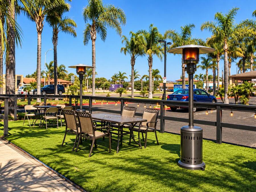 An outdoor patio with tables and chairs, surrounded by palm trees and a street view.