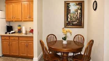 A dining area with a wooden table and chairs, a coffee maker, and a painting on the wall.