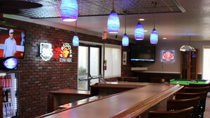 Una zona de bar con mesa de billar, letreros de neón y una pantalla de televisión.