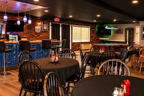 A bar area with a pool table, multiple seating arrangements, and a television screen.