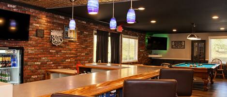 A bar area with a pool table, seating, and a brick wall with a television.