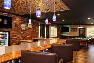 Zona de bar con mesa de billar, asientos y pared de ladrillo con televisor.