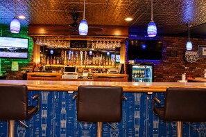 A bar area with a counter, bar stools, a television screen, and a beer fridge. - O'cairns Inn & Suites (Lompoc)