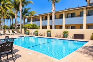 A hotel pool area with a clear blue pool, lounge chairs, and potted plants. - O'cairns Inn & Suites (Lompoc)