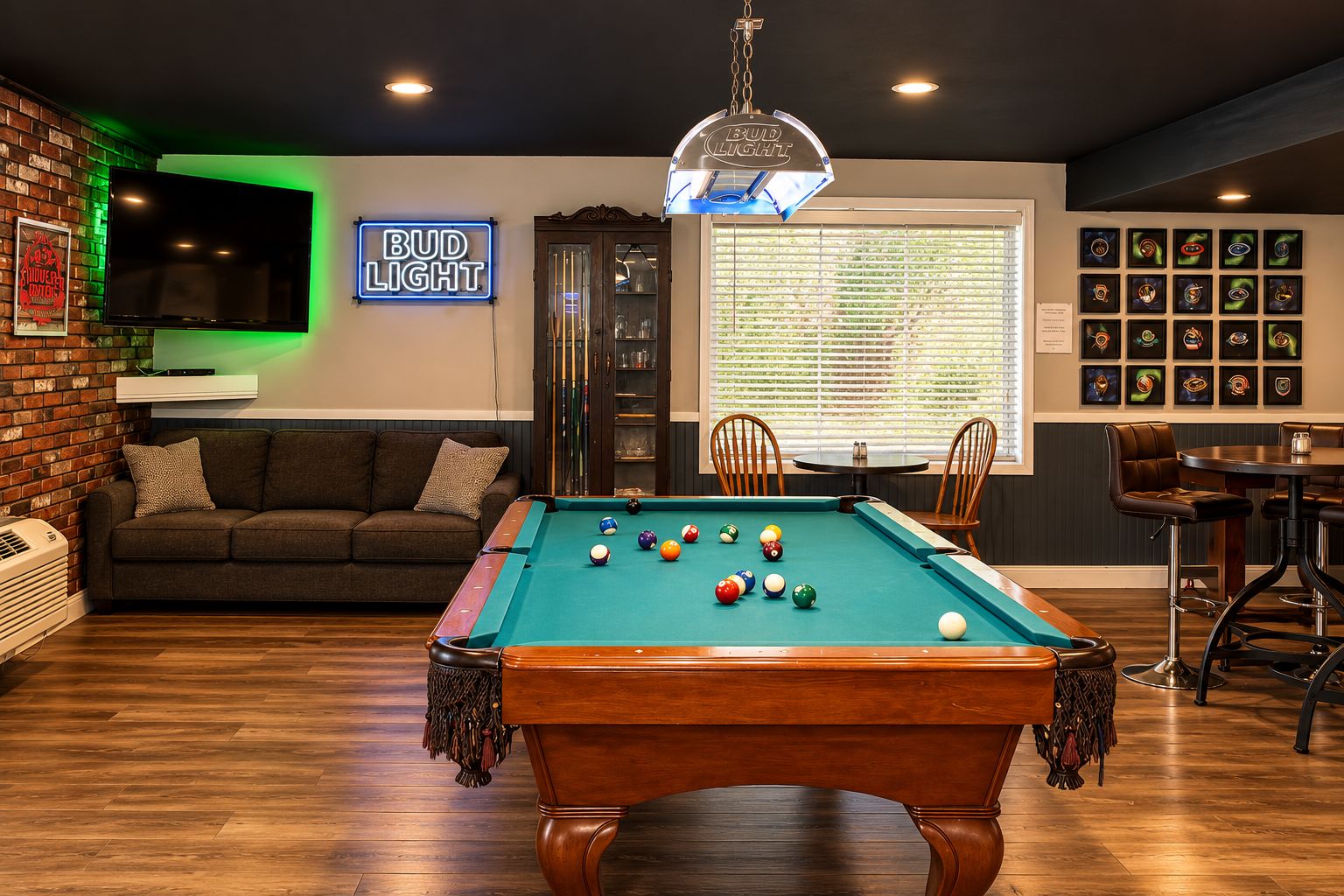 A pool table in a room with a sofa, a neon sign, and framed pictures on the wall.
