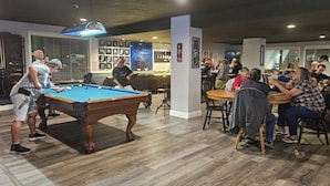 Una mesa de billar en una sala con barra y cuadros en las paredes.