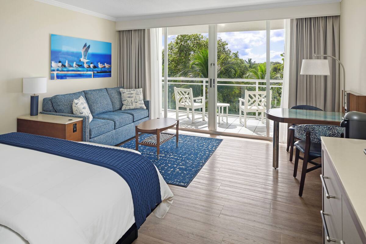 Ein Hotelzimmer mit Bett, einer Couch, einem Schreibtisch und einem Balkon mit Stühlen.