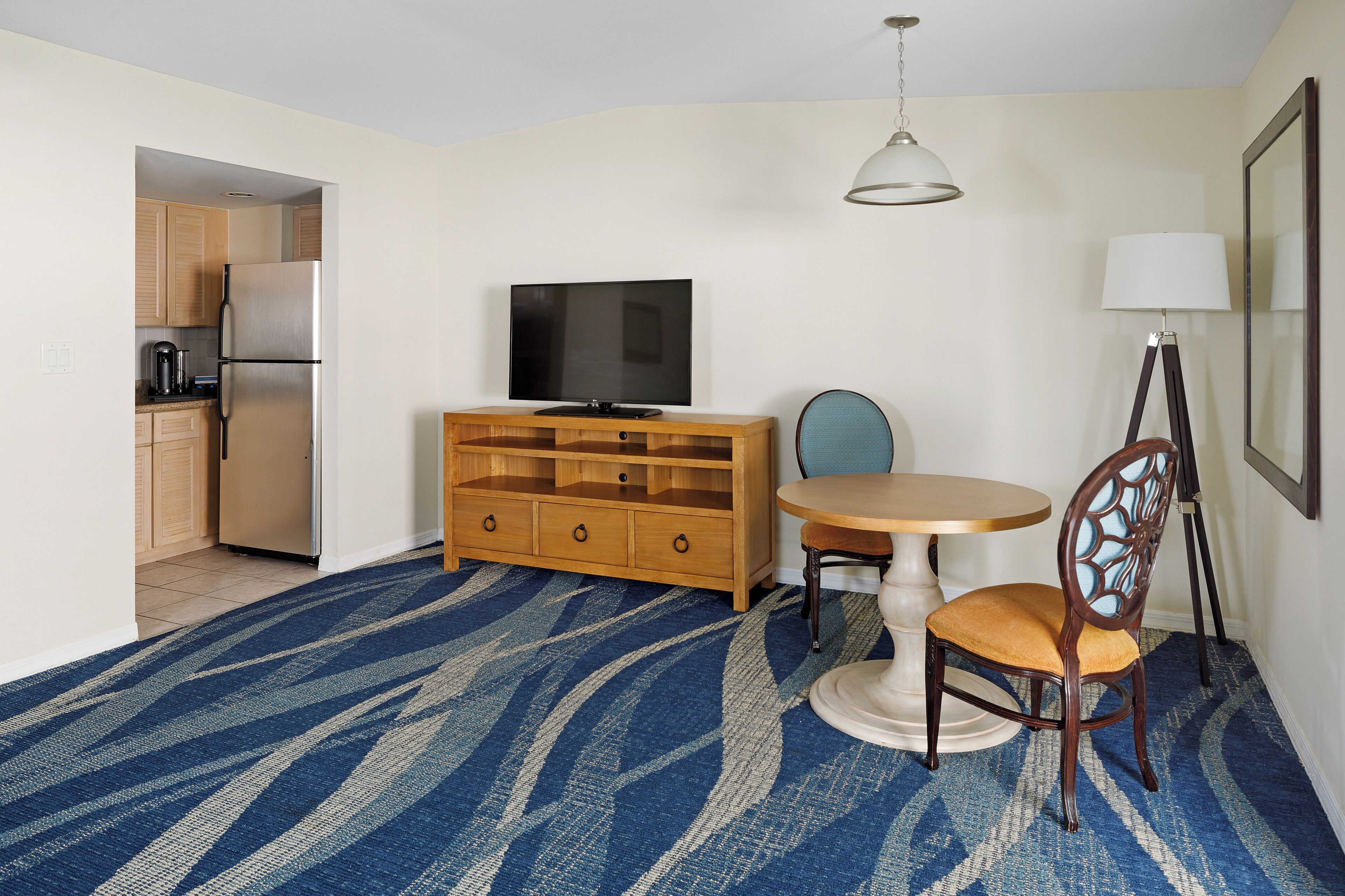 A compact living space with a kitchenette, a television, a dining table with a chair, and a lamp.
