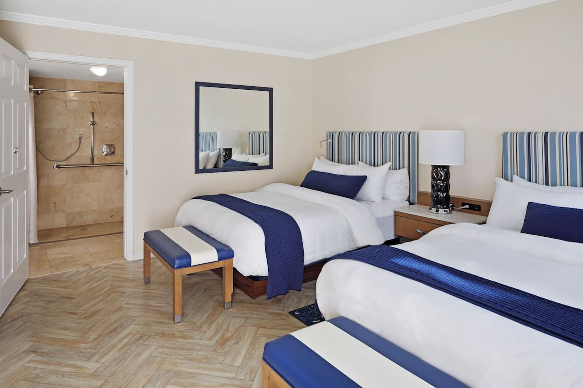 Ein Hotelzimmer mit zwei Betten, einer Duschkabine, einer Sitzbank und einem Nachttisch mit Lampe.