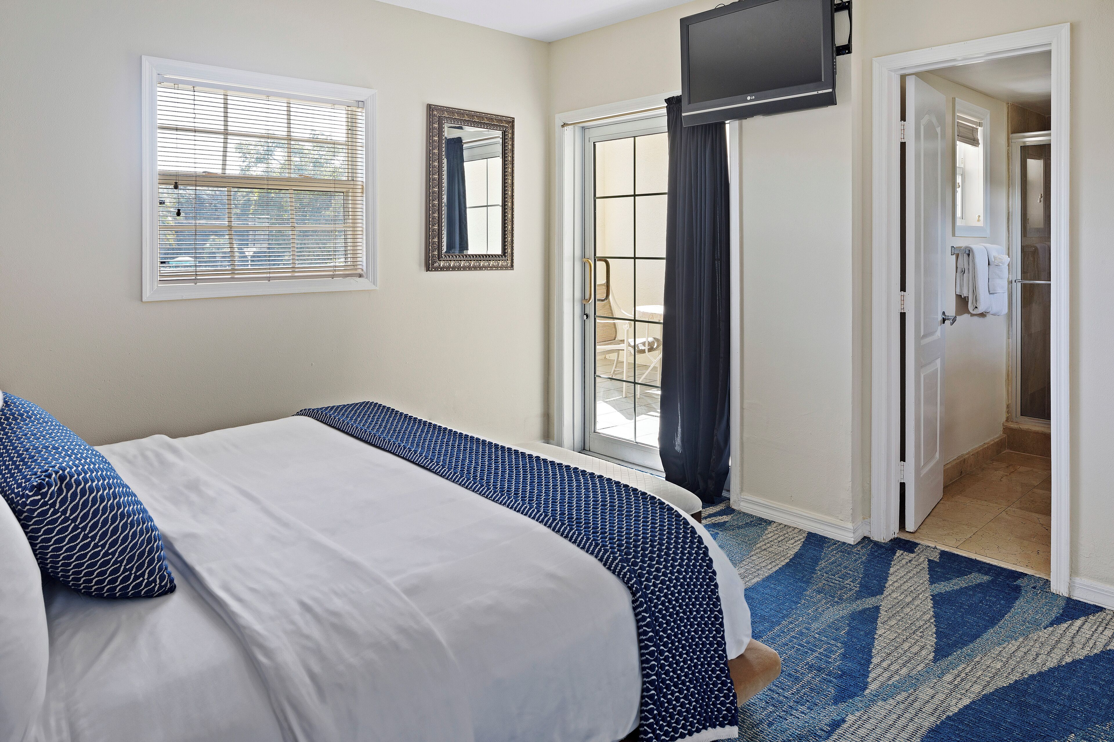 A bedroom with a bed, a window with blinds, a mirror, and a door leading to a bathroom.